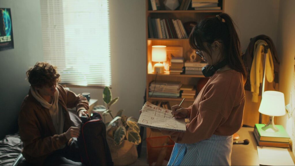 A woman working on a storyboard while a man packs filming gear